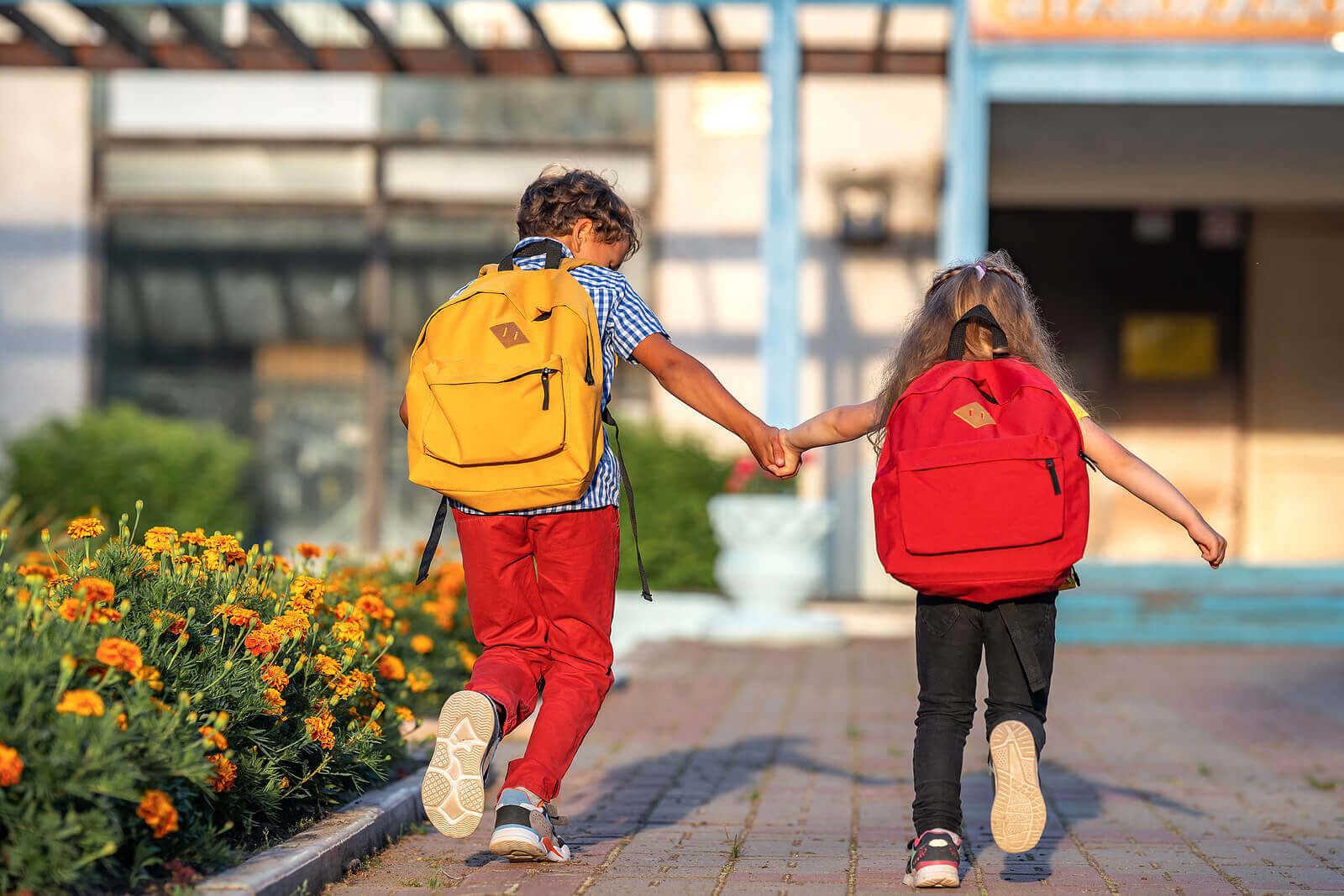 Image of two children holding hands and wearing backpacks while running to school. Discover how effective child therapy in Thousand Oaks, CA can be to help support your child with their emotions.
