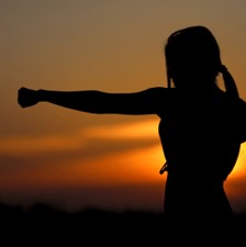 A silhouette of a woman with her fist raised at sunset.