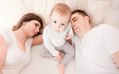 A man and woman are laying on a bed with a baby. A man and woman are laying on a bed with a baby.