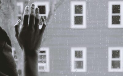 A grayscale image of a person's hands pressed against a rain-spattered window
