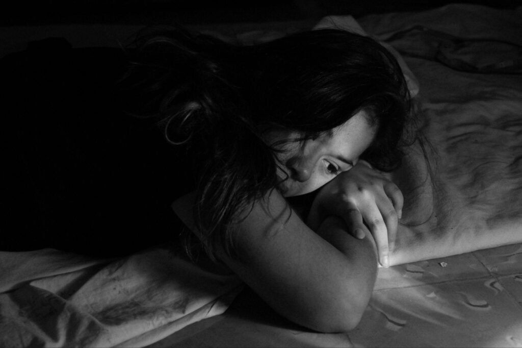  Black and white photo of a woman lying down on a bed with a pensive expression