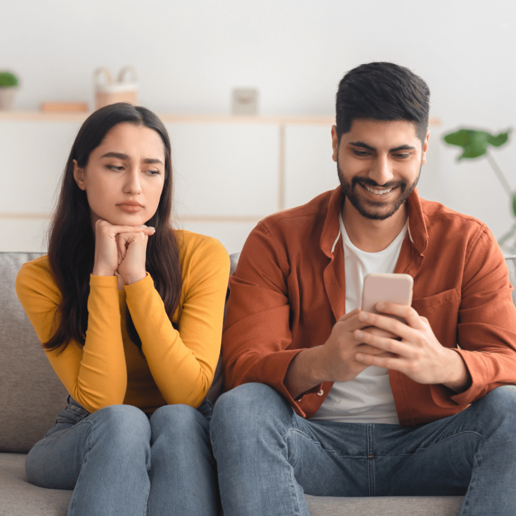 A man and woman are seated on a couch, both absorbed in their smartphones, illustrating contemporary social interaction.