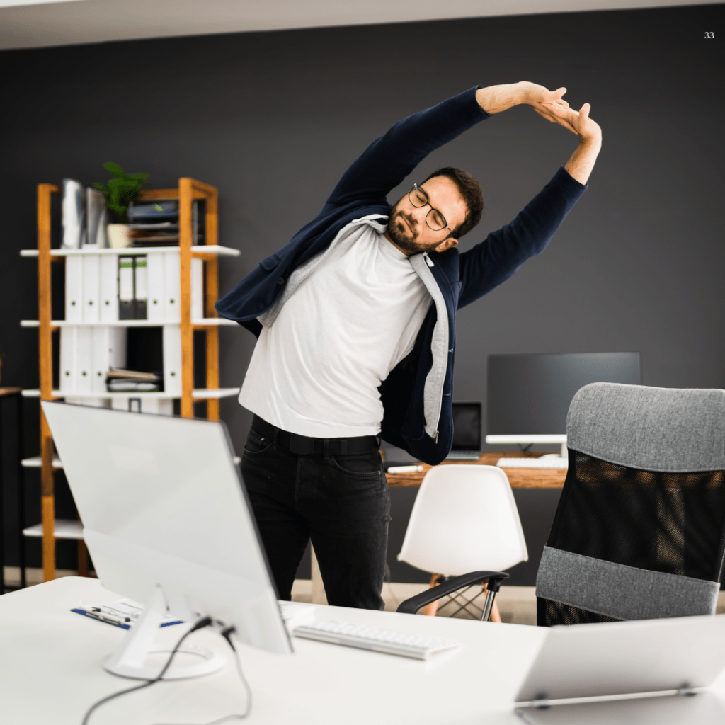 A man performing a stretching exercise in front of a computer, promoting wellness and flexibility during work hours.