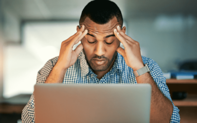 A man sits at a desk, visibly distressed, with his head resting in his hands, conveying a sense of frustration or overwhelm.