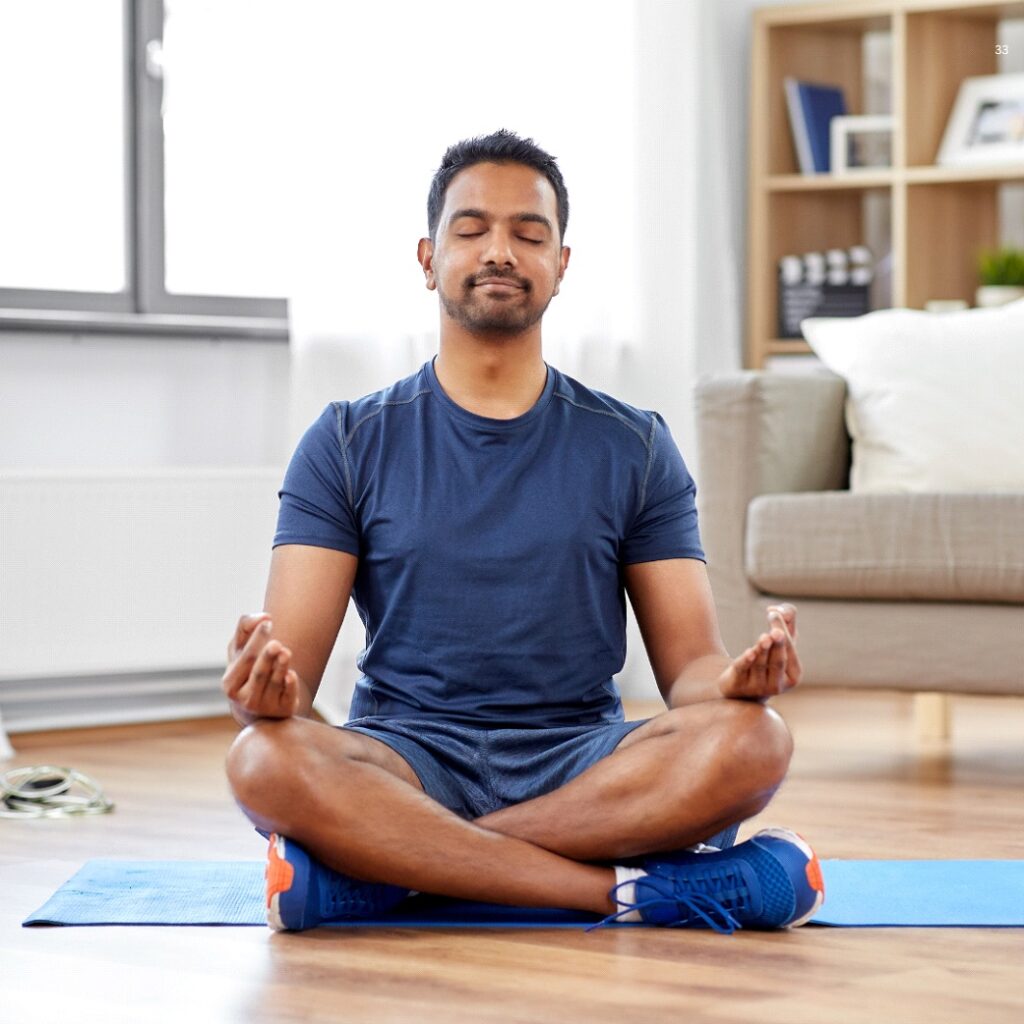 A Person with Closed Eyes Is Sitting Cross-Legged on a Mat in a Sunny Room, Practicing Meditation.