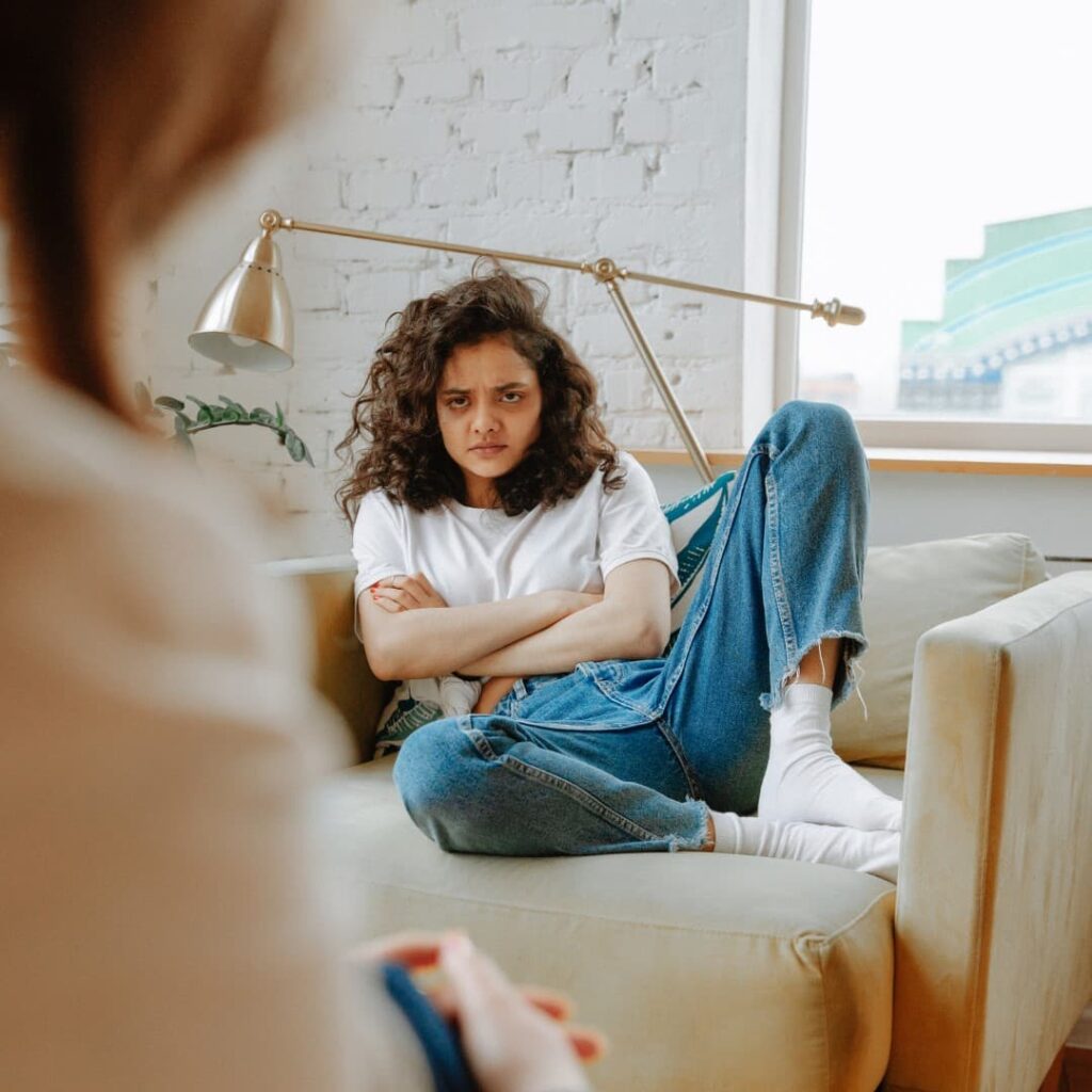 A person with curly hair, wearing a white shirt and jeans, looking at an out-of-focus figure in the foreground.