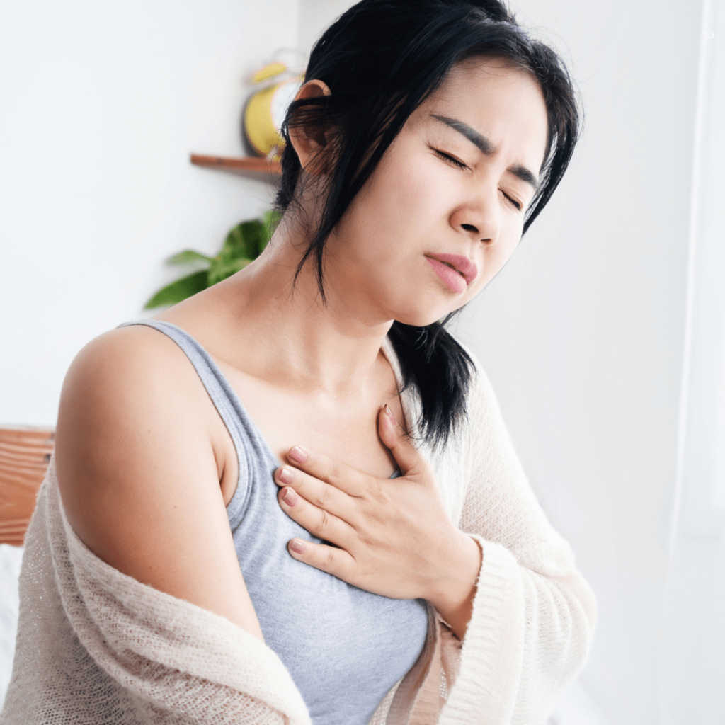 A woman experiencing chest pain while lying in bed, her hand on her chest, reflecting a state of distress and concern.