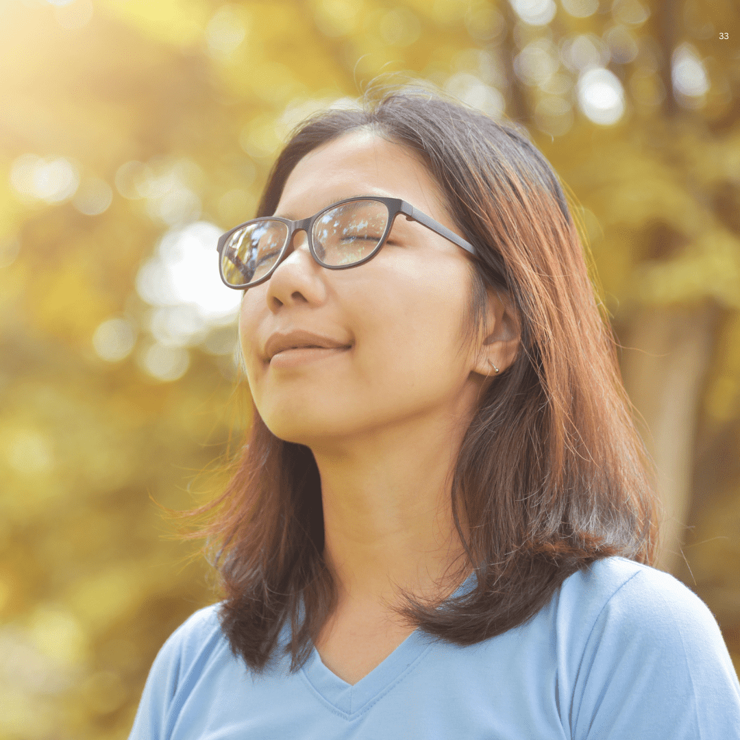 A woman with glasses, showcasing a thoughtful expression, stands against a neutral background, emphasizing her features.