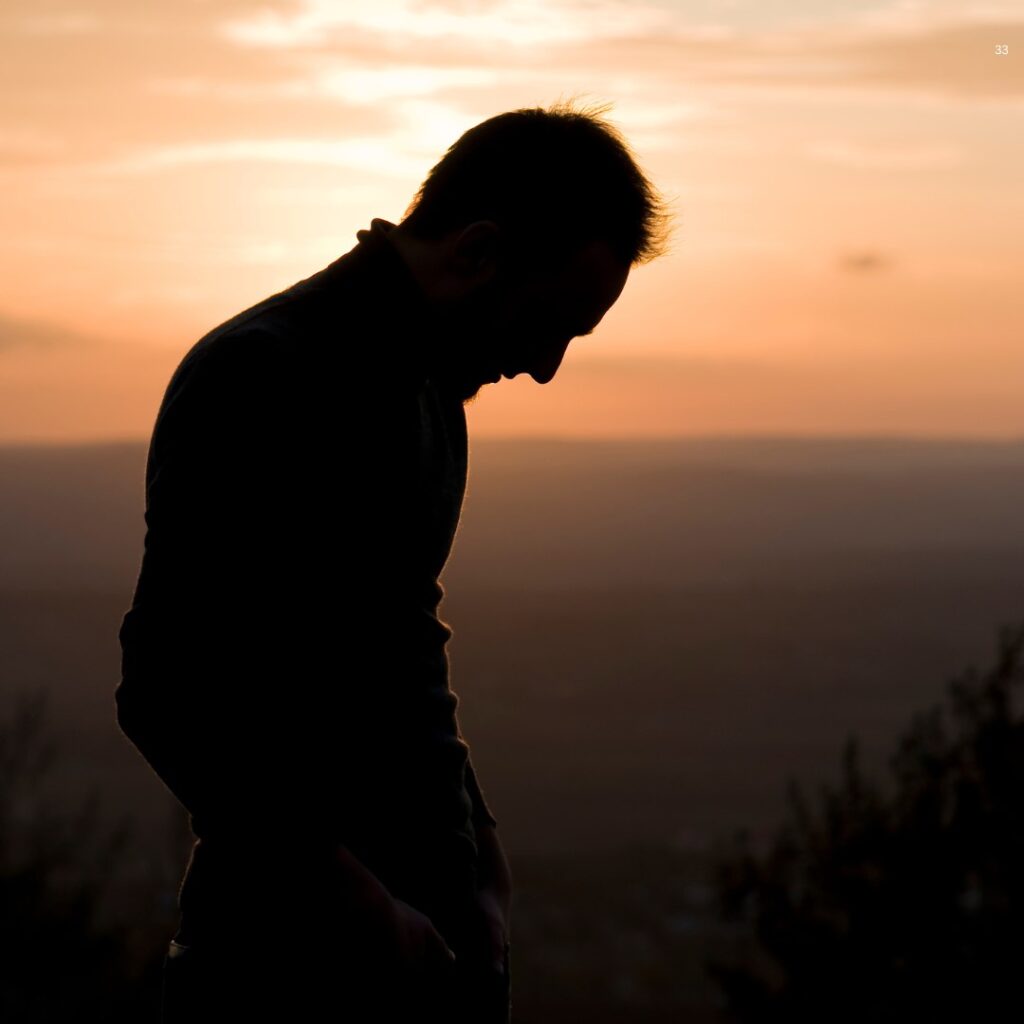 Silhouetted man standing outdoors at sunset, looking down.