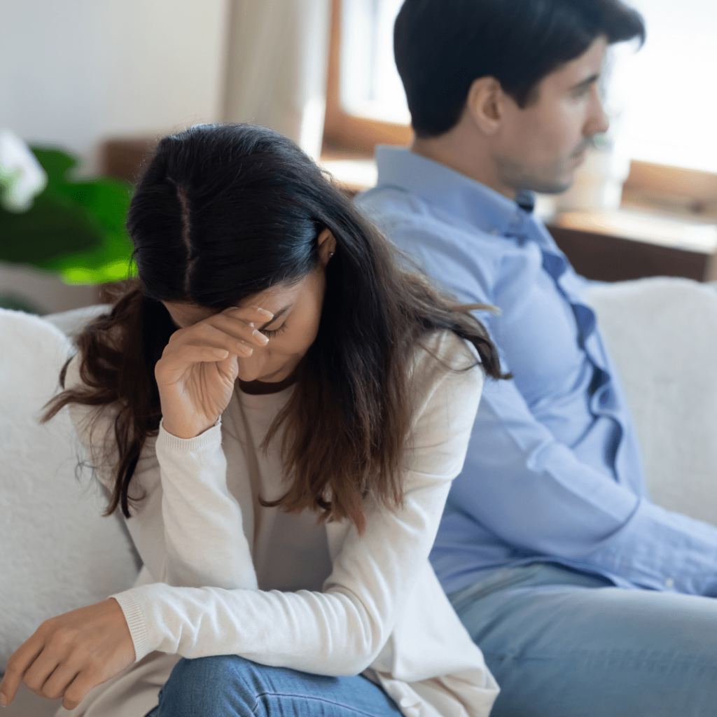 Two people sitting apart on a sofa in a room, suggesting tension or disagreement.