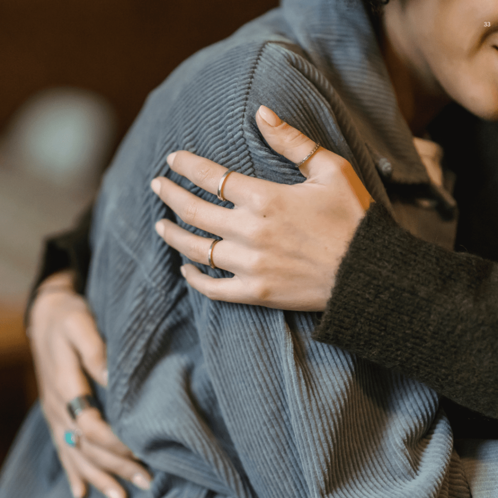 Two women share a heartfelt hug, both dressed in soft sweaters, symbolizing warmth and emotional support.