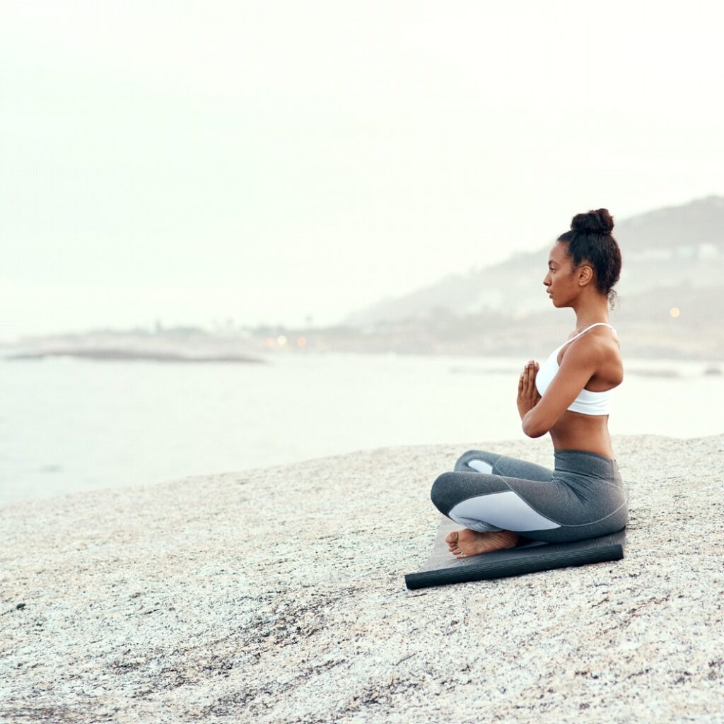 Woman Meditating on a Rocky Shoreline, Sitting Cross-Legged on a Yoga Mat