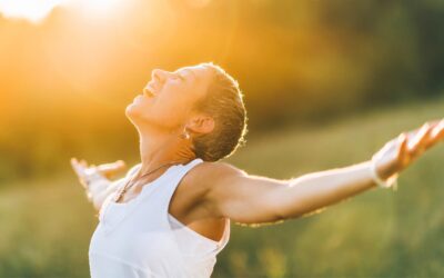 Woman with Short Hair Smiling with Arms Outstretched, Standing in a Sunlit Field, Enjoying the Warm Golden Light.