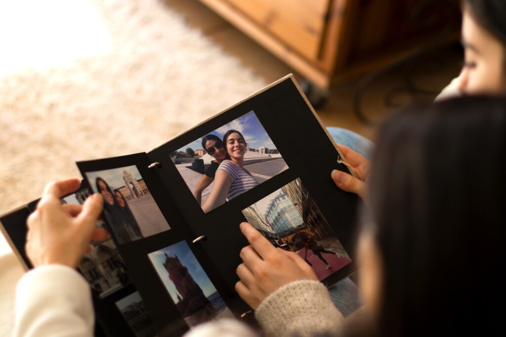 Two women examine photographs in a book, sharing smiles and memories as they engage in a meaningful conversation.