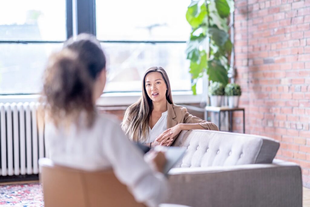 A woman seated on a couch engages in conversation with another woman, both appearing attentive and engaged.