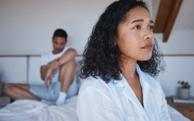 A woman and a man sitting together on a bed, engaged in conversation and sharing a moment of connection.