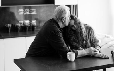 An older couple sitting together at a kitchen table, engaged in conversation and enjoying each other's company.