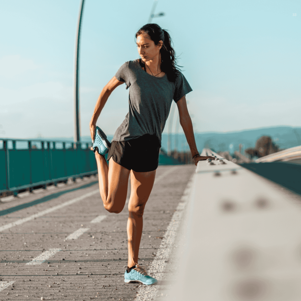 a woman stretching her leg on a bridge before or after a run. She is dressed in athletic clothing