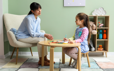 A psychiatrist or therapist sitting with a child. The child is smiling at the therapist with a marker in her hand.